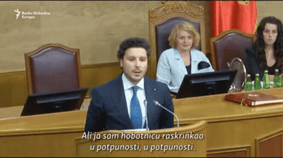 Man in Suit Giving Speech at Podium Saying Ali
