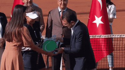 Man In Suit Giving Tennis Racket To Woman In White Visor GIF