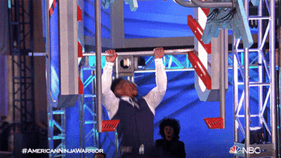 Man In Suit Hanging Upside Down On Bar With NBC Logo GIF