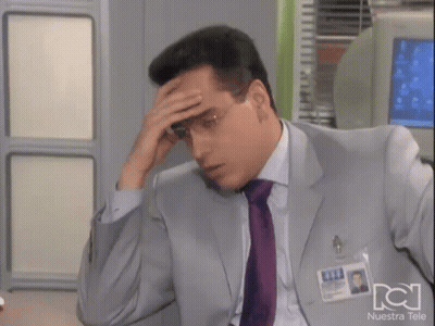 Man In Suit Holding Forehead In Front Of Nuestra Tele Sign GIF