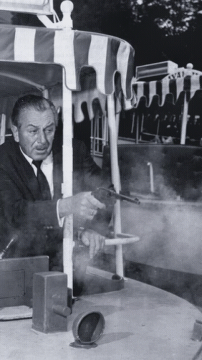 Man In Suit Holding Gun By Striped Canopy GIF
