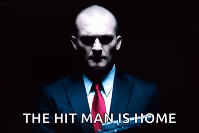Man In Suit Holding Gun Saying The Hit Man Is Home GIF