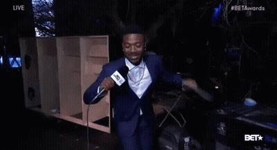 Man In Suit Holding Microphone And Smiling On Stage GIF