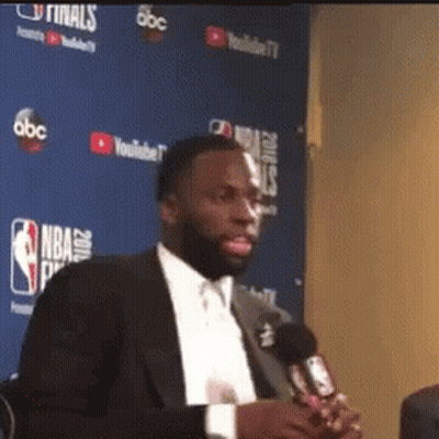 Man In Suit Holding Microphone At Blue Wall Saying NBA GIF