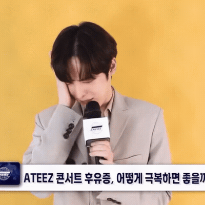 Man In Suit Holding Microphone In Front Of ATEEZ Sign GIF