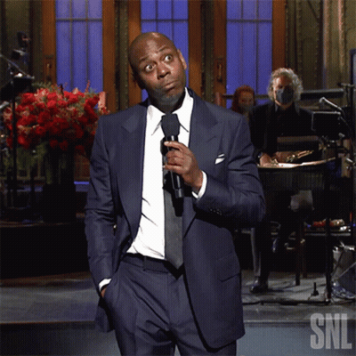 Man In Suit Holding Microphone In Front Of SNL Logo GIF
