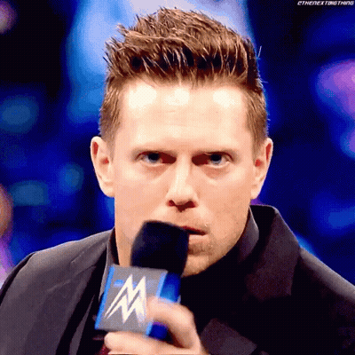 Man In Suit Holding Microphone With Letter M GIF