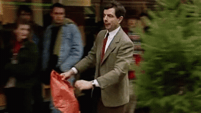 Man In Suit Holding Red Bag Next To Christmas Tree GIF
