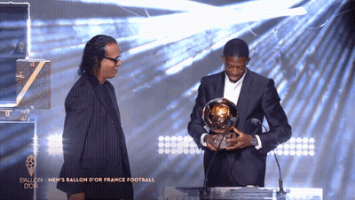 Man in Suit Holding Trophy at Microphone Saying Ballon d'Or