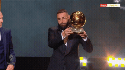 Man In Suit Holding Trophy In Front Of Direct Equipe Screen GIF
