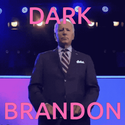 Man In Suit In Front Of Dark Brandon Sign GIF