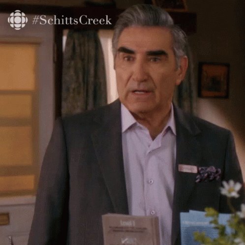 Man In Suit In Front Of Schitt's Creek Sign GIF