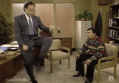 Man In Suit Jumping On Chair Beside Seated Man GIF