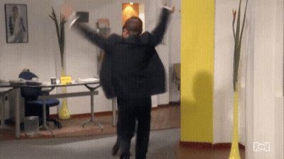 Man In Suit Jumping With Arms Outstretched In Office GIF