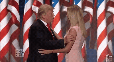 Man In Suit Kissing Woman In Pink Dress On Stage With American Flags GIF