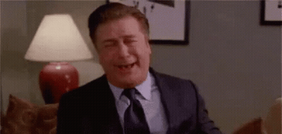 Man In Suit Laughing Eyes Closed On Couch GIF