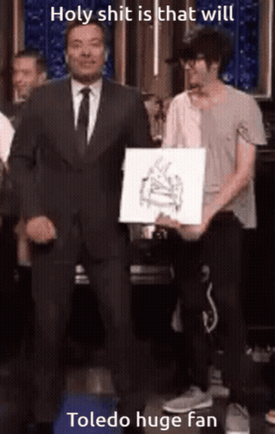 Man In Suit Next To Man Holding Toledo Huge Fan Paper GIF