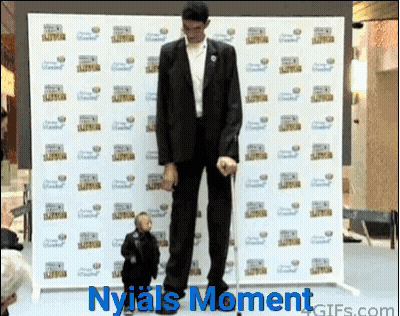 Man in Suit Next to Smaller Man in Front of Nyjais Moment Wall