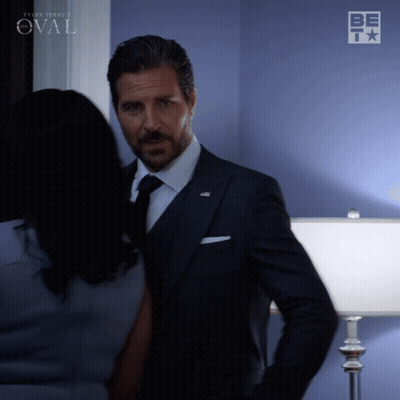 Man In Suit Next To Woman By Blue Wall Saying Oval GIF