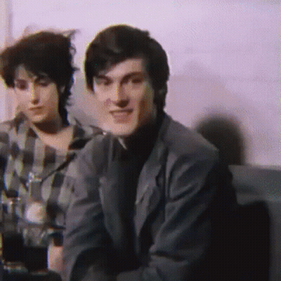 Man In Suit Next To Woman In Plaid Shirt On Couch GIF