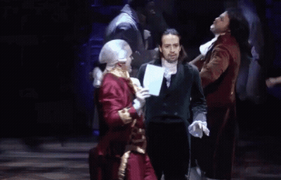 Man In Suit On Stage In Front Of Men In Costume GIF