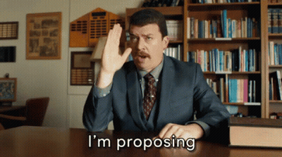 Man In Suit Proposing In Front Of Bookshelf GIF
