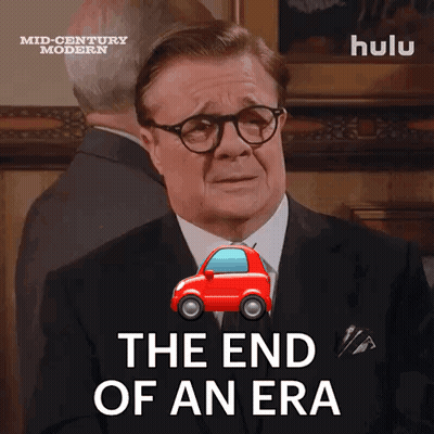 Man in Suit Says The End of an Era Next to Red Car