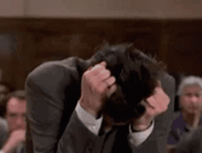 Man In Suit Scratching Head In Crowded Room GIF