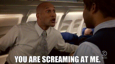 Man In Suit Screaming At Another Man On Airplane GIF