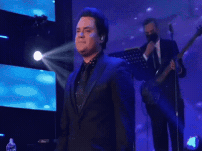 Man In Suit Singing Onstage With Guitarist GIF