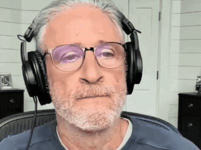 Man In Suit Sitting At Desk In Front Of Comedy Central Screen GIF