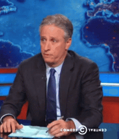 Man In Suit Sitting At Desk In Front Of Comedy Central Screen GIF