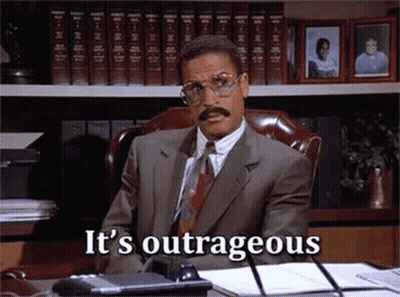 Man In Suit Sitting At Desk With Bookshelf GIF
