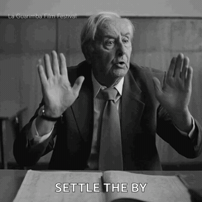 Man In Suit Sitting At Desk With Hands Up Saying Settle GIF