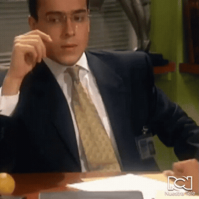 Man In Suit Sitting At Desk With Nuestra Tele Logo GIF