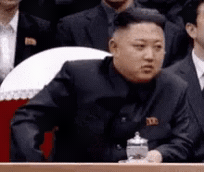 Man In Suit Sitting At Podium In Front Of Crowd GIF