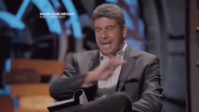 Man In Suit Sitting At Shark Tank Sign GIF