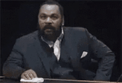 Man In Suit Sitting At Table Says Ah Bon GIF