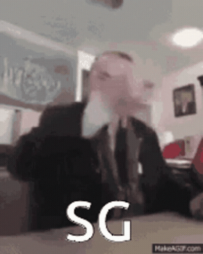 Man In Suit Sitting At Table With SG On Screen GIF