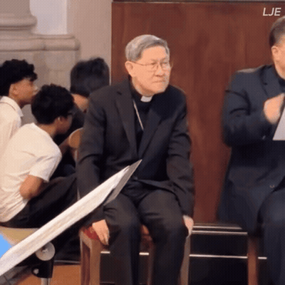 Man In Suit Sitting Before Group With LJE Above GIF