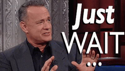 Man In Suit Sitting In Front Of Just Wait Sign GIF