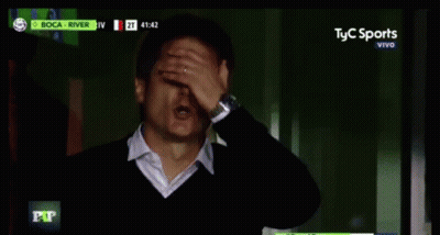 Man In Suit Sitting In Front Of Screen Saying El Nueve Vivo GIF