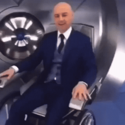 Man In Suit Sitting In Wheelchair Holding Remote GIF