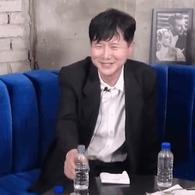 Man In Suit Sitting On Blue Couch Holding Water GIF