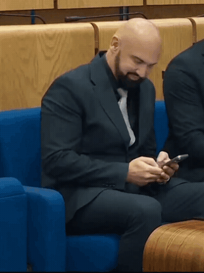 Man In Suit Sitting On Blue Couch Looking At Phone GIF