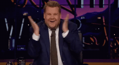 Man In Suit Sitting On Stage With Hands In Air GIF
