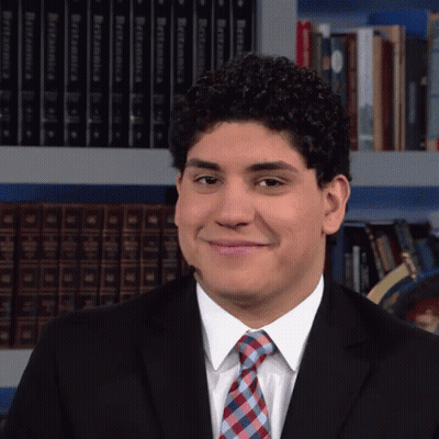 Man In Suit Smiling Before Bookshelf With Dictionary GIF