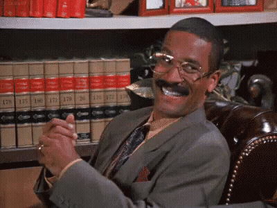 Man In Suit Smiling In Front Of Bookshelf GIF