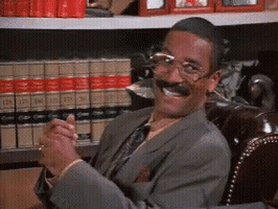 Man In Suit Smiling In Front Of Bookshelf GIF