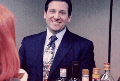 Man In Suit Smiling In Front Of Liquor Bottles GIF